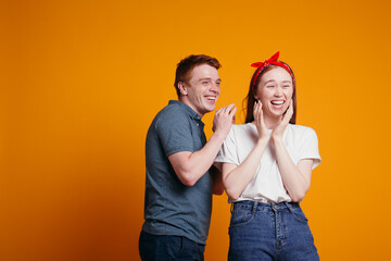Red-haired guy and girl laughing while shooting in the studio on an orange background.