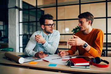 Young male coworkers discussing ideas for common project brainstorming together in office, skilled...