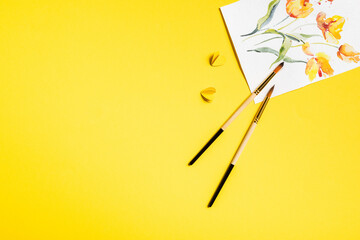 top view of paintbrushes near drawn flowers on painting and paper cut elements on yellow
