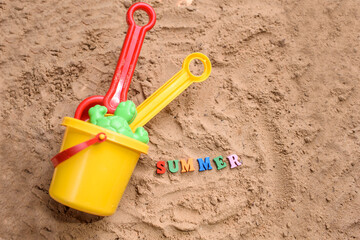 Fototapeta na wymiar Beach sand with toys for the baby, water, the word summer in colored letters.