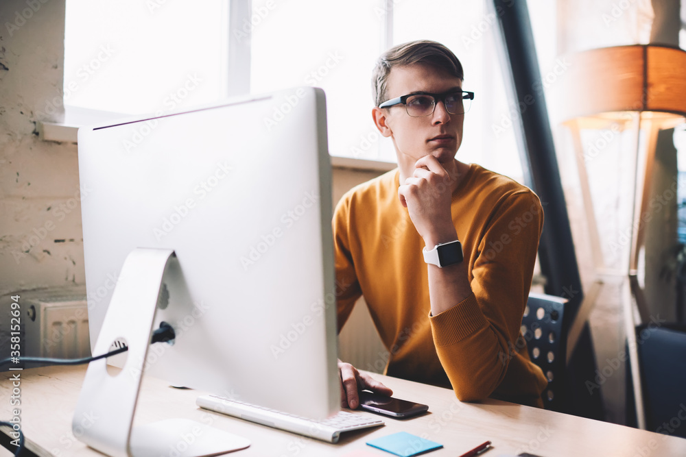 Poster caucasian hipster guy pondering on wireless connection on computer staying on office desktop, young 