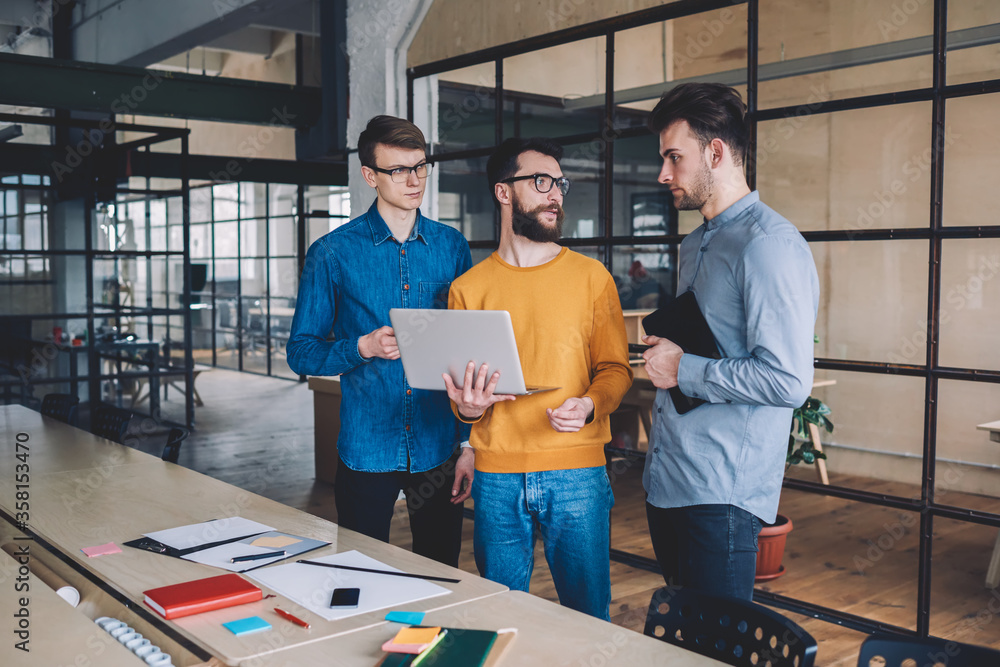 Poster caucasian male employees discussing ideas for solution using laptop computer for searching informati