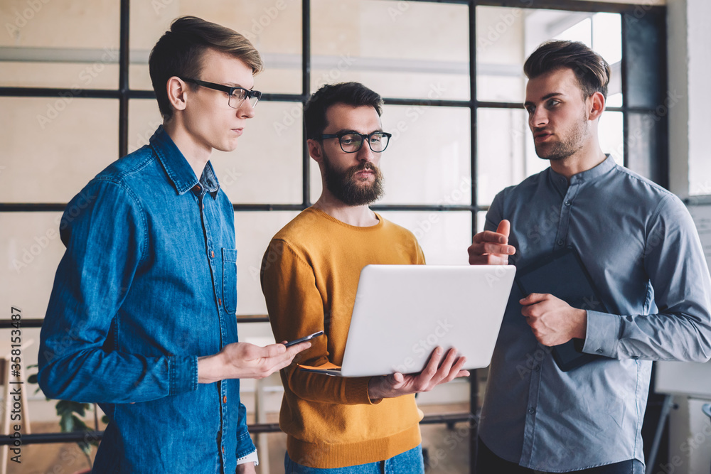 Poster group of young hipster guys downloading file on laptop device while browsing 4g internet, caucasian 