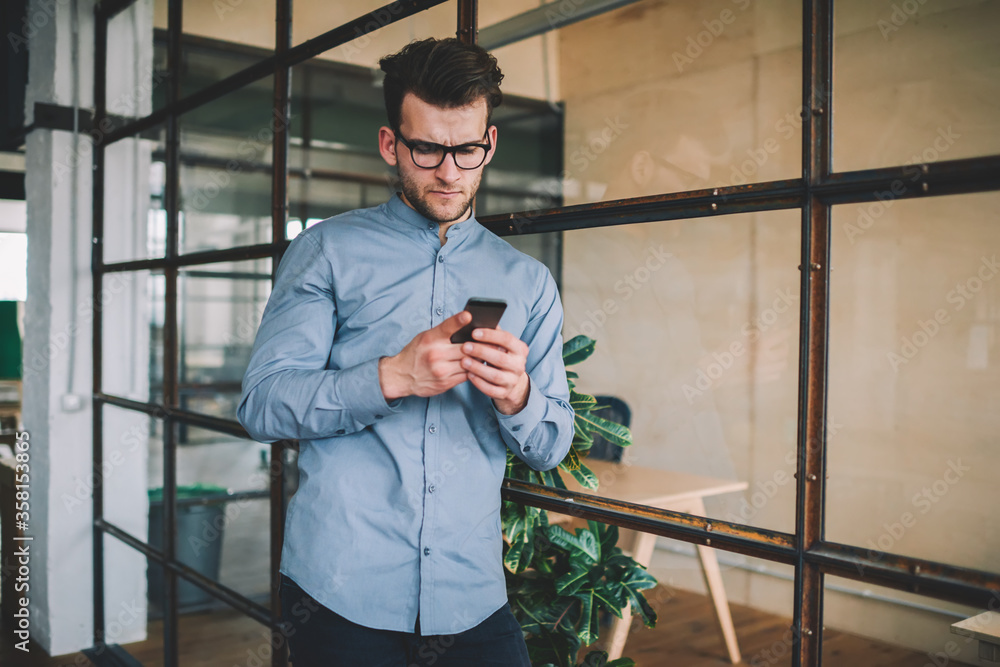 Poster perplexed caucasian man reading sms message via smartphone device browsing internet indoors, confuse