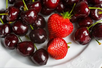 Glossy cherries on a white plate with red strawberries. Ripe and juicy cherry fruits and strawberries