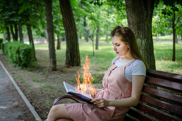 A young beautiful girl sits on a park bench and reads a book. Flames erupted from an open book