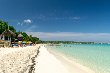 People/ tourists on Seven Mile Beach in Negril, Jamaica coast on sunny summer vacation day. Beautiful tropical Caribbean island holiday scene. Rasta color glass bottom boat docked.