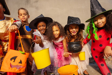 Many kids hold Halloween candy buckets and smile looking to the camera - Powered by Adobe