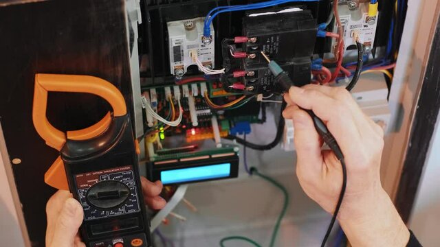 Electricians hands testing current  electric in control panel. Electrician engineer work  tester measuring  voltage and current of power electric line in electical cabinet control.