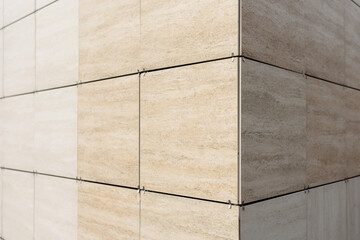 The wall of the building with beige ceramic tiles. The corner of the building, perspective