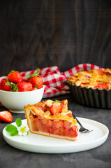 Pie with rhubarb and strawberries on a dark wooden background with fresh strawberries. Vertical orientation, copy space.