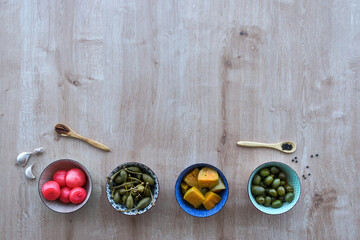 Fototapeta na wymiar Assorted pickles: aubergines, olives, spring onions and capers in bowls on a wooden surface, top view, copy space.