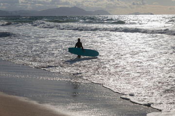 Fototapeta na wymiar Surfer girl carrying their surfboard in the beach, ready to surf