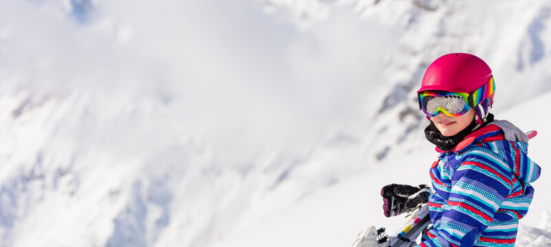 Close portrait of smiling girl in ski outfit color mask and pink helmet high in the mountains