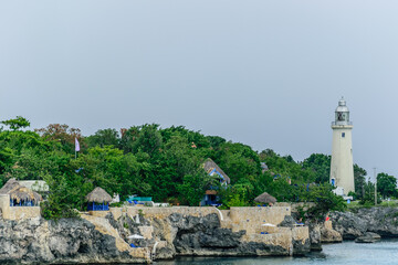 The Negril Lighthouse beside a cliffside hotel resort on the coast of Negril, Jamaica. Thatch roof cottages for vacationers/ tourists with ocean views.