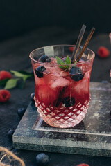 Glass of cold red alcohol cocktail decorated with ice, fruit, flowers and mint on table at the bar.