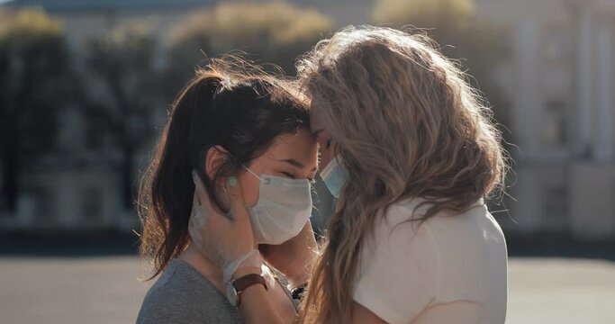 Two multi-racial lesbians kiss through a mask outside in the sun, end of quarantine. LGBT
