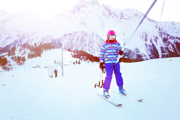 Girl in a colorful outfit on the ski drag lift bar smiling and holding sticks in hand
