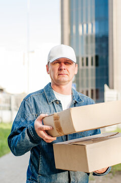 male courier in the blue costume and a cap taking out mail carton boxes from the white van on the sunny day in the street. Outdoor.
