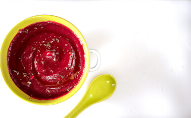 Beetroot soup in a bowl  and a green spoon on a white table. Top view. Copy space at right