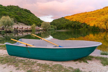 A turquoise boat stands on the shore against the lake. The lake is surrounded by hills, they grow forest. A place equipped for fishermen, fishing in a beautiful place, boat rides, romance, trip.