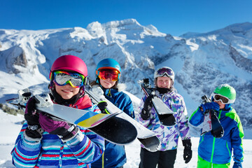 Portrait of a smiling cute girl in pink helmet and color googles hold ski in her hands in a group of friends children over mountain