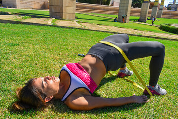 Female model training the buttocks in the park, using elastic bands