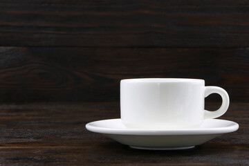 A cup of coffee on a brown wooden background. White coffee cup and saucer. Copy space. Place for text.