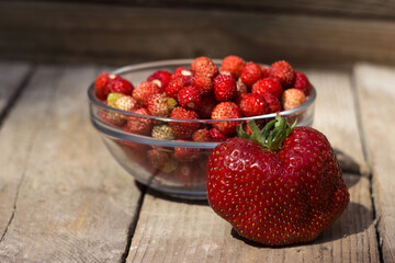 Big strawberry and full ripe strawberries in a glass plate on a wooden background. Useful red berries.