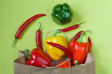 Fresh sweet peppers and red, yellow and green chili peppers in a paper bag on a green background. Bag for shopping. Top view.