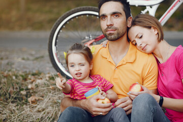 Family in a park. People with a bicycle. Parents with little daughter. People have a snack.