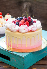 Pink cake with melted chocolate, strawberry, blueberry and cherry and cupcakes with whipped cream and fresh berries.