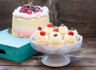 Pink cake with melted chocolate, strawberry, blueberry and cherry and cupcakes with whipped cream and fresh berries.