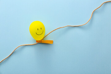 Air balloon with drawn happy face, rope and peg on color background