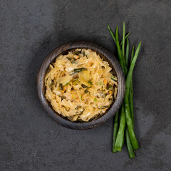 Cabbage stewed with carrots and green onions in a wooden bowl on a dark background top view