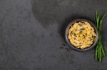 Cabbage stewed with carrots and green onions in a wooden bowl on a dark gray background top view copy space