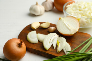 Fototapeta na wymiar Board with cut onion and garlic on white wooden table