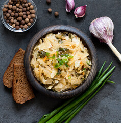 Cabbage stewed with carrots and green onions in a wooden bowl on a dark gray background top view