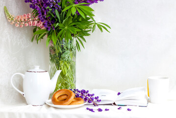 Sweet bagels and tender lupine flowers. Light composition with bright and purple flowers. A gentle and romantic morning with tea and a book. A book of poems for Breakfast.