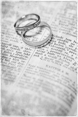 Wedding rings in black and white lying on the text of the Bible.