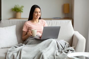 Fototapeta premium Woman With Laptop Having Coffee Sitting On Couch At Home