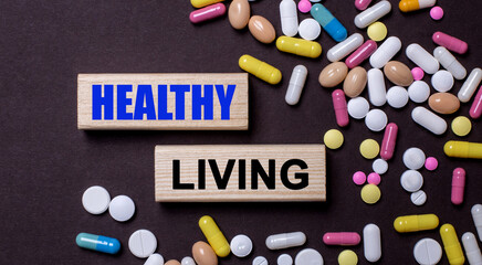 Healthy lifestyle is written on wooden blocks that stand on a dark background between multi-colored pills