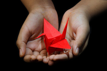 Hand holding Origami Paper Crane (Orizuru), Red bird.  on Black Background 