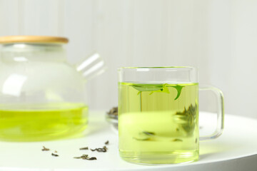 Cup of aromatic green tea with leaves on white table