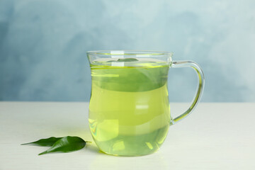 Cup of aromatic green tea and leaves on light wooden table
