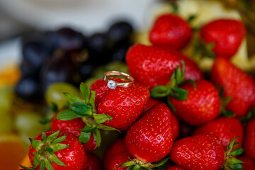 The wedding ring lies on a red ripe strawberry. Summer delicious berries
