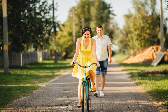 Portrait of attractive woman with stylish haircut and retro look riding on old bicycle and smiling at camera. Man is behind the woman on rode. Hot summer day.