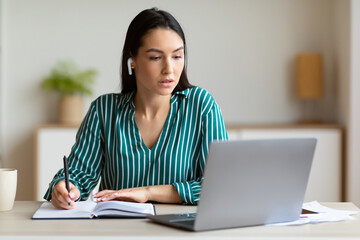 Woman At Laptop Taking Notes Combining Work And Study Indoors