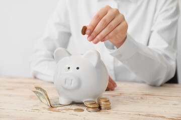 Woman putting money in piggy bank on table
