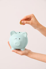 Woman putting money in piggy bank on light background